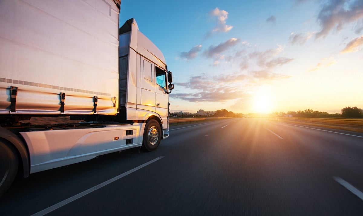 A truck driving on an asphalt road at sunset