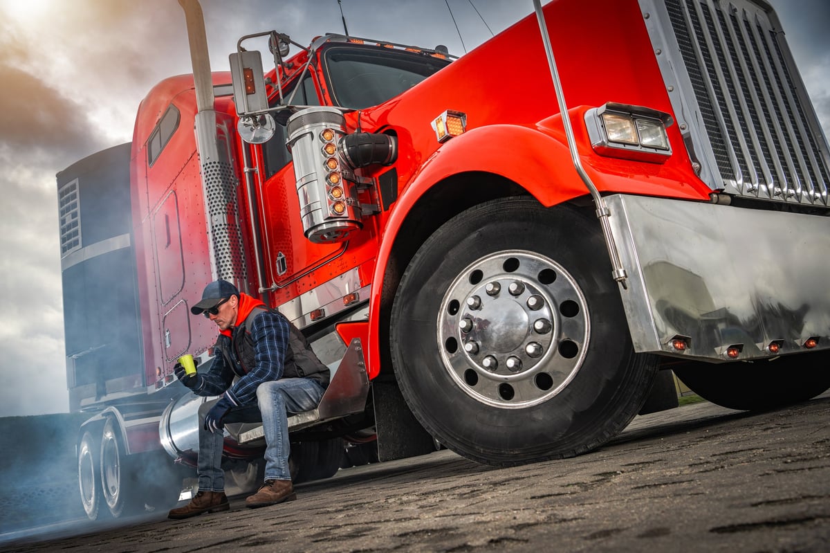 A truck driver taking a break beside a red truck