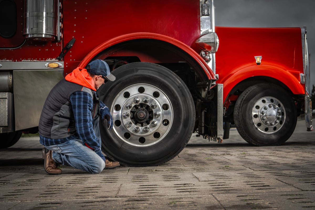 A driver checking the tire pressure on a red truck