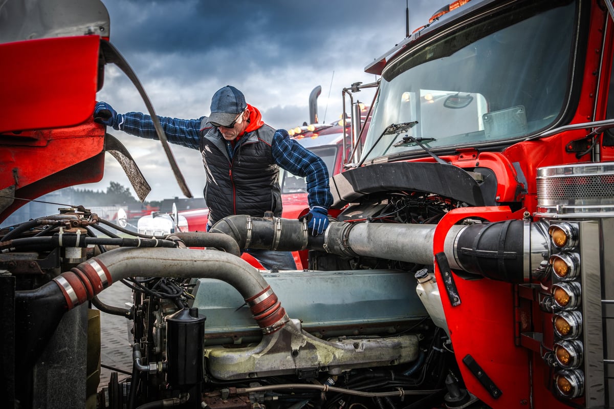A mechanic repairing the engine of a red truck in a trucking yard