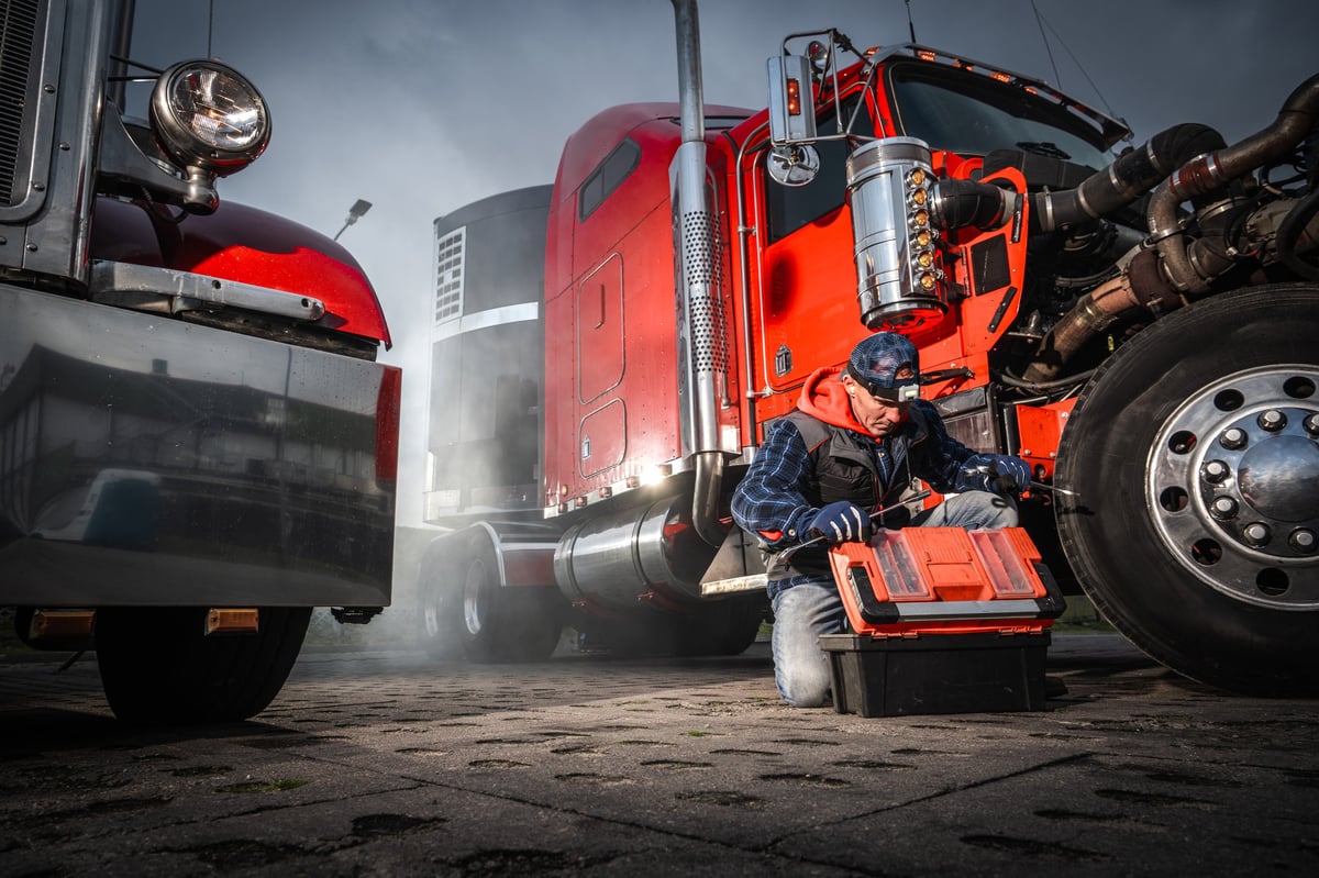 A mechanic crouched beside a truck in a busy yard